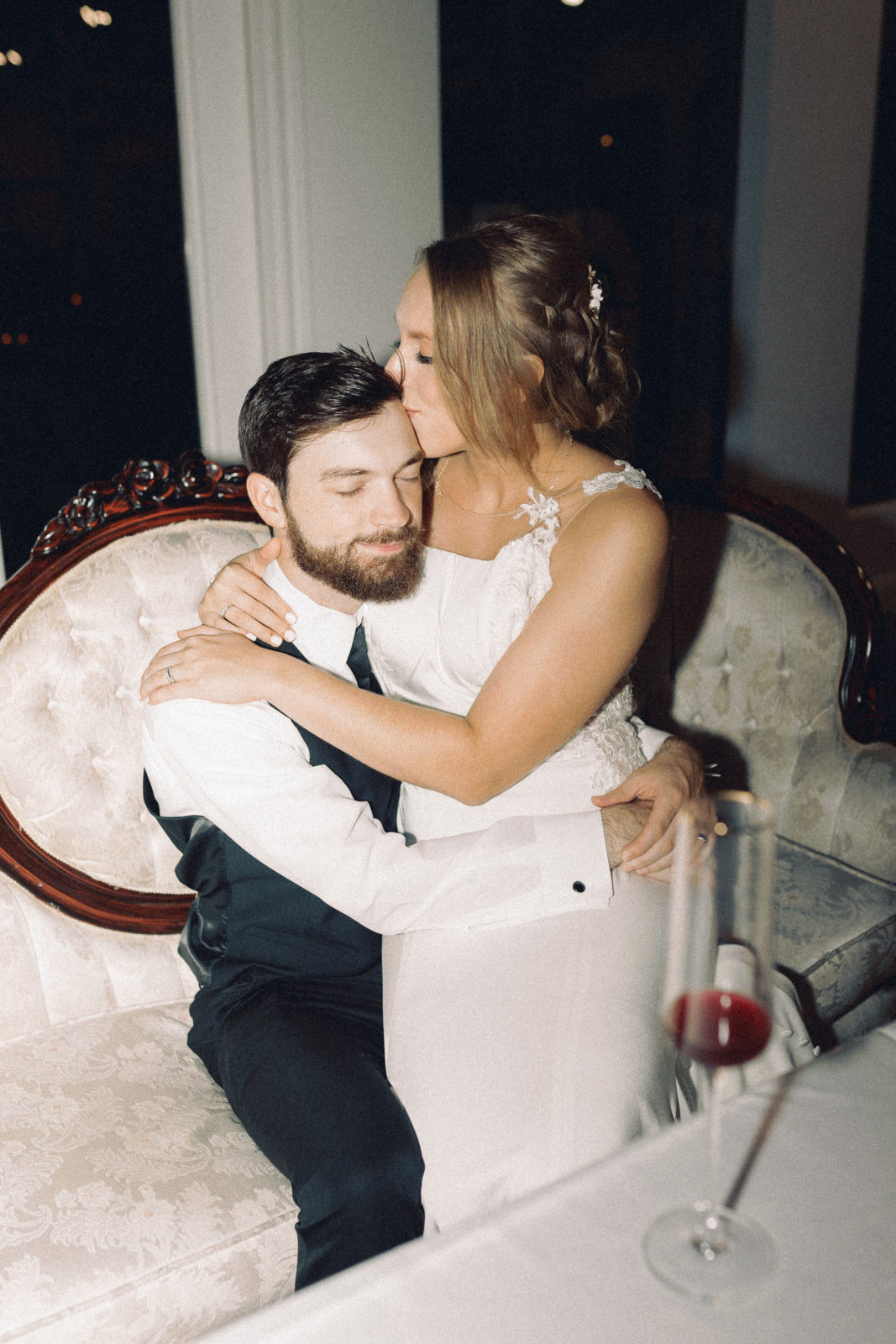 bride sitting on grooms lap, kissing his forehead